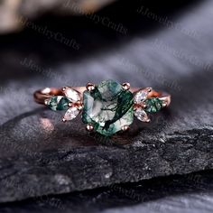 a green and white diamond ring sitting on top of a black stone slab with leaves around it