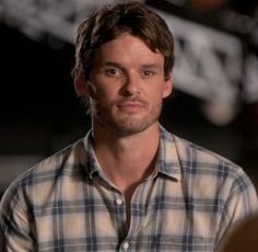 the young man is wearing a plaid shirt and looking to his left with an intense look on his face