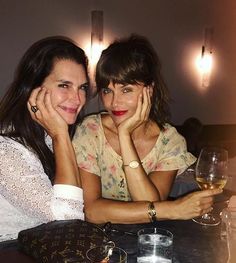 two women sitting next to each other at a table with wine glasses in front of them