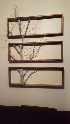 three wooden frames are hanging on the wall with a tree in it and branches sticking out of them