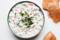 a bowl filled with dip and crackers on top of a white table next to two pieces of bread