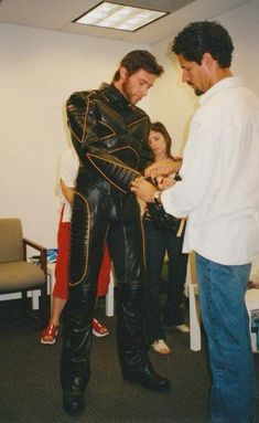 two men in black leather suits standing next to each other and one man wearing white shirt