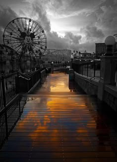 a pier with a ferris wheel in the background and clouds reflecting on the water at sunset