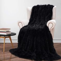 a chair with a black blanket on top of it next to a table and books