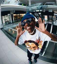 a woman wearing sunglasses and a t - shirt is standing in front of an escalator