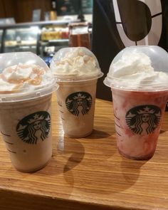 three starbucks drinks sitting on top of a wooden table