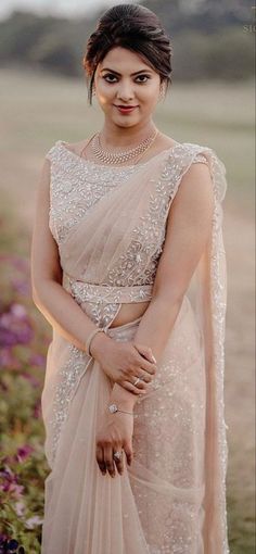 a woman in a beige sari posing for the camera with her hands on her hips