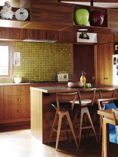 a kitchen with wooden cabinets and chairs around a table in front of an island that has two green apples on it