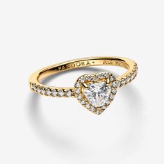 Radiate love in our Elevated Heart Ring featuring a symbolic heart-shaped clear cubic zirconia, set in a 14k gold plating with a pavé halo. Its raised stone and claw setting highlight the eye-catching centre, while half of the ring shank is adorned with pavé. Perfect for adding a touch of love to any outfit, this ring captures the essence of heartfelt connections. - Pandora Elevated Heart Ring - 14k Gold-plated unique metal blend / Cubic Zirconia / Clear - Sz. 7.5 Promise Ring Pandora Gold, Unique Promise Rings For Her Gold, Pandora Gold Heart Ring, Pandora Gold Jewelry, Gold Pandora Ring, Pandora Gold Rings, Pandora Elevated Heart Ring, Gold Promise Rings For Her, Gold Pandora Rings