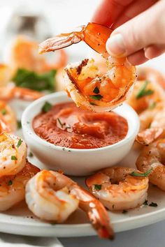 a person dipping sauce onto shrimp on a plate