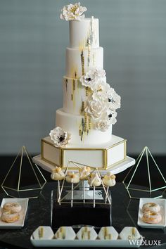 a white and gold wedding cake sitting on top of a table next to pastries