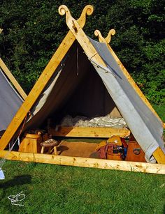 a tent made out of wood and canvas in the middle of some grass with other items around it