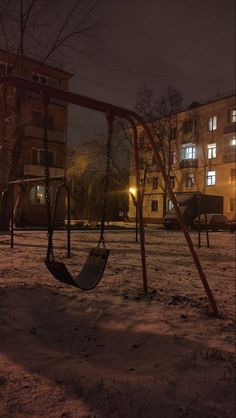 an empty swing set at night in a snowy park with no one on the swings