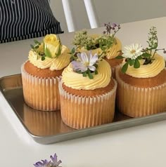 three cupcakes with yellow frosting and flowers on top sitting on a tray