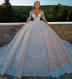 a woman in a wedding dress standing on a stone wall with her hands on her hips