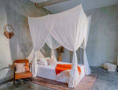 a bed with white drapes and orange pillows