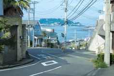 an empty street next to the ocean with power lines in the air and houses on both sides