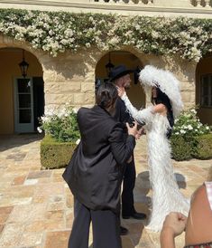 a man in a feathered suit and top hat standing next to a woman wearing a long white dress