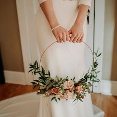 a woman in a white dress holding a basket with flowers and greenery on it