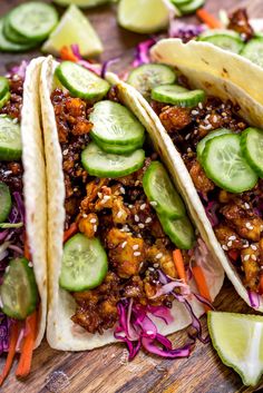 three tacos with cucumbers, carrots and red cabbage on a cutting board