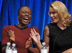 two women laughing while sitting in front of a blue curtain and talking to each other