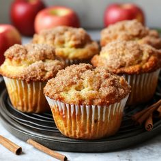 some muffins are sitting on a plate with cinnamon sticks and apples in the background