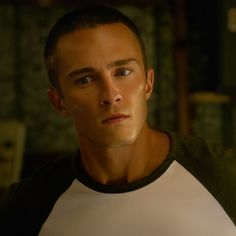 a man in a white and black t - shirt looking at the camera with an intense look on his face