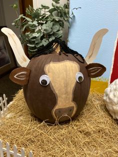 a fake cow head sitting on top of hay next to a fence and potted plant