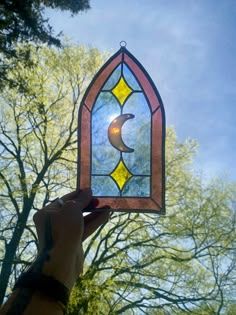 a hand holding up a stained glass window with the moon in it's center