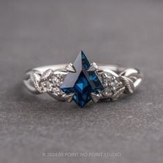 a blue diamond ring sitting on top of a gray surface with vines around the band