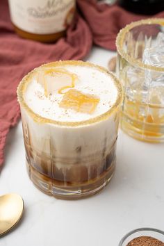 two glasses filled with liquid sitting on top of a table next to bottles and spoons