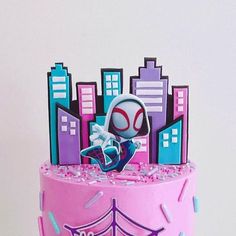 a pink cake with spiderman on top and city skyline in the background, topped with sprinkles