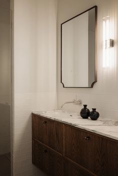 a bathroom vanity with two black vases on it and a large mirror over the sink