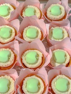 there are many cupcakes with green frosting on them in pink paper wrappers