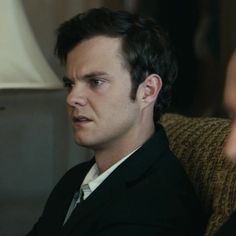 a man in a suit and tie sitting on a chair looking at another man's face