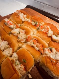 a wooden cutting board topped with lots of bread covered in shrimp and crab meats