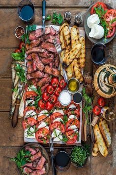 an assortment of food is laid out on a wooden table with utensils and plates