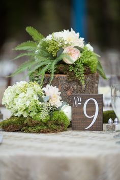 flowers and greenery are arranged on the table number 9, which sits next to a wooden block