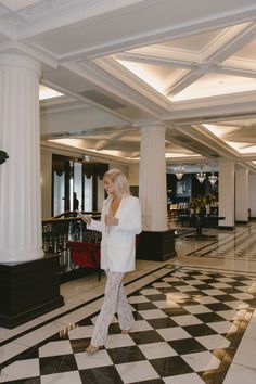 a woman in white is walking down the hall with black and white checkered floor