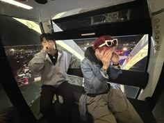 two people sitting on top of a building looking at the city from inside an observation tower