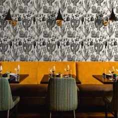 the interior of a restaurant with yellow booths and cactus wallpaper, along with green chairs