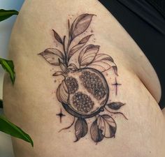 a woman's thigh with a tattoo on it that has a pomegranate and leaves