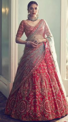 a woman in a red and gold lehenga standing by a window with her hands on her hips