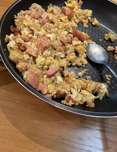 a frying pan filled with food on top of a wooden table next to a spoon