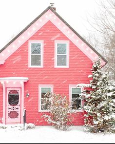 a pink house with christmas lights on the front door and trees in the snow behind it