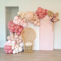 balloons and flowers are on display in front of a baby's breath sign with a wicker chair next to it