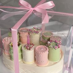 there are many cakes in the box with pink ribbons on it's sides and one is decorated with flowers