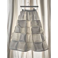 a dress hanging on a hanger in front of white curtains with grey and white squares