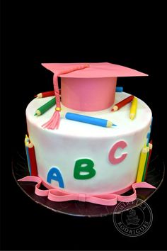 a white cake with pink frosting and colorful writing on the top has a mortar, pencils, and graduation cap