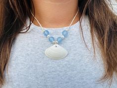 a woman wearing a blue and white beaded necklace with a shell pendant on it